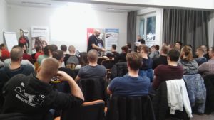 Na zdjęciu widać uczestników wydarzenia, którzy siedzą tyłem do kamery. Ich postawy i ułożenie sugerują, że są skupieni na tym, co dzieje się przed nimi.