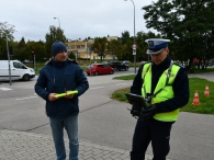 policjant z pracownikiem WORD w Białymstoku trzymającym opaski odblaskowe koloru seledynowego, obsługuje kontroler kamery drona